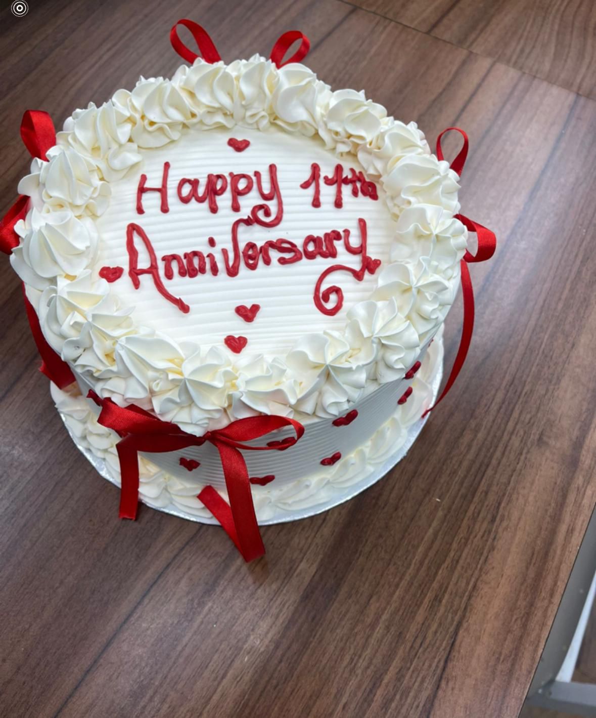 Anniversary cake with white frosting, red ribbons, and 'Happy Anniversary' text on a wooden surface.