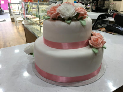 Two-tiered wedding cake with pink ribbon and flowers in a store setting