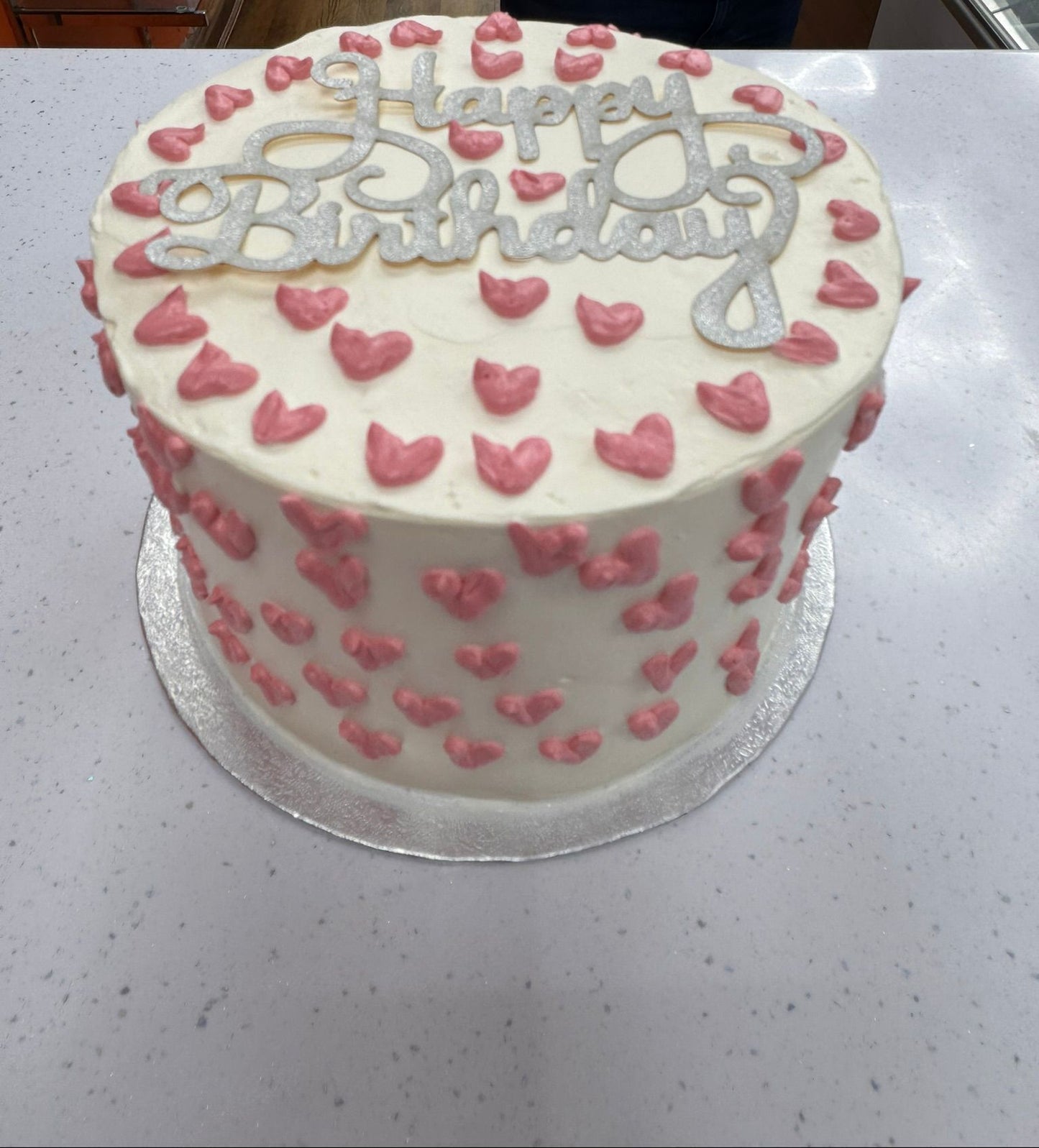 White birthday cake with pink hearts and 'Happy Birthday' text on a white surface.