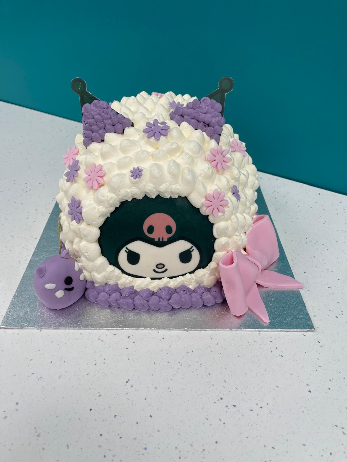 Decorative cake with cartoon character face, purple flowers, and pink bow on a white surface.